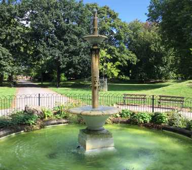 Planted borders and mown grass around an ornamental fountain in a public park